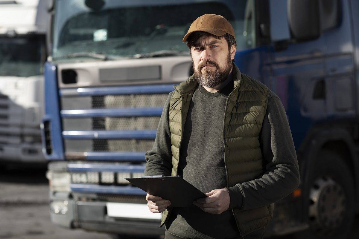 gestão de frota - homem com uma prancheta com folhas na mão, à frente de um caminhão de cabine azul
